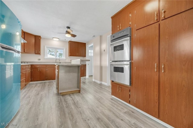 kitchen featuring ceiling fan, sink, stainless steel double oven, light hardwood / wood-style floors, and a kitchen island