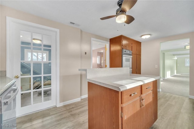 kitchen with visible vents, brown cabinets, light wood finished floors, light countertops, and baseboards