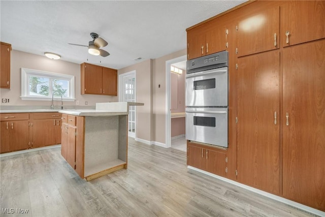 kitchen with light countertops, brown cabinets, light wood-style floors, stainless steel double oven, and a sink