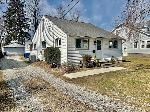 view of front of property featuring an outbuilding, a front yard, driveway, roof with shingles, and central air condition unit