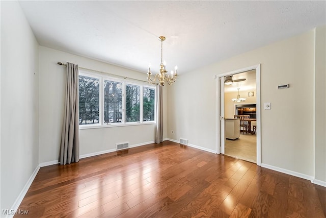 empty room with visible vents, baseboards, an inviting chandelier, and wood finished floors