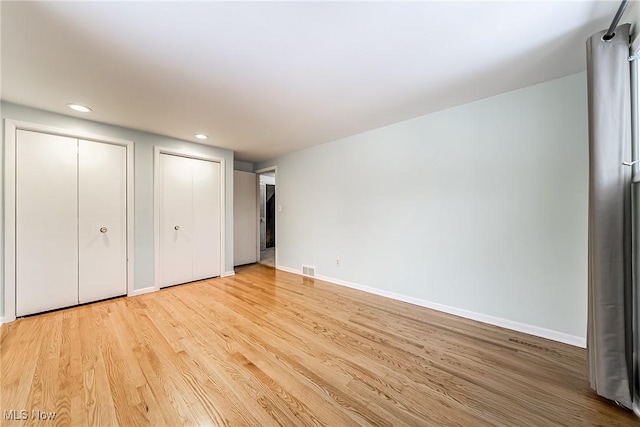 unfurnished bedroom with visible vents, two closets, recessed lighting, light wood-style floors, and baseboards