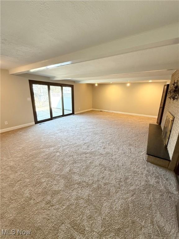 unfurnished living room featuring beamed ceiling, carpet flooring, baseboards, and a textured ceiling