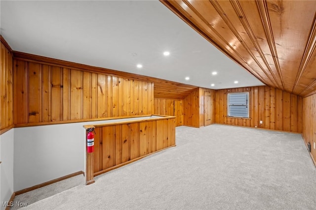 interior space featuring light carpet, wooden walls, and lofted ceiling