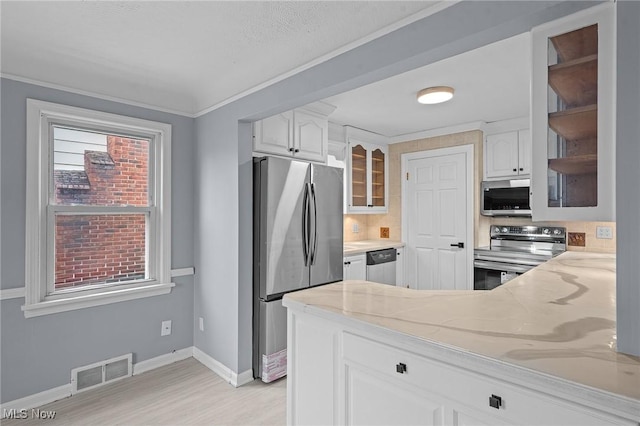 kitchen with light stone counters, white cabinetry, ornamental molding, and appliances with stainless steel finishes