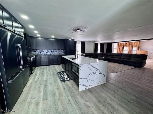 kitchen featuring decorative backsplash, light hardwood / wood-style floors, light stone counters, and appliances with stainless steel finishes