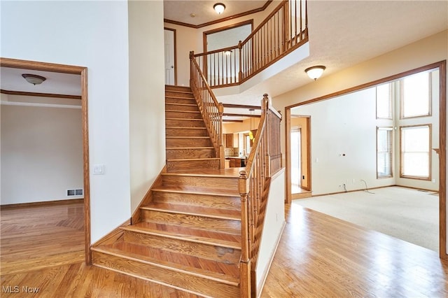 staircase with hardwood / wood-style floors, a towering ceiling, and ornamental molding