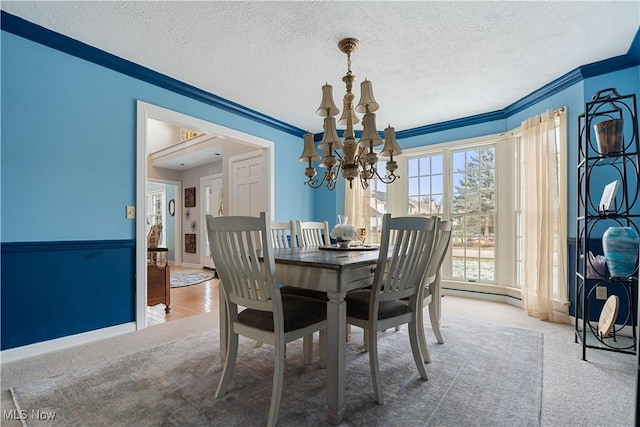 carpeted dining room featuring ornamental molding, a textured ceiling, and a notable chandelier