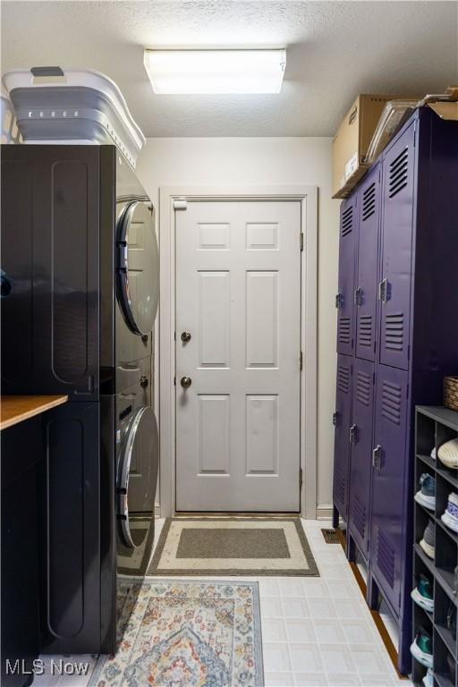 clothes washing area with stacked washing maching and dryer and a textured ceiling