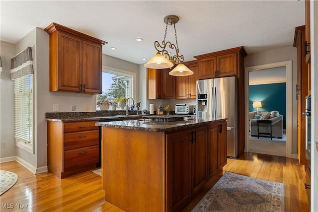 kitchen with decorative light fixtures, light hardwood / wood-style flooring, dark stone countertops, stainless steel fridge with ice dispenser, and a center island