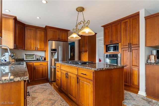 kitchen with sink, stainless steel appliances, light hardwood / wood-style flooring, dark stone counters, and decorative light fixtures