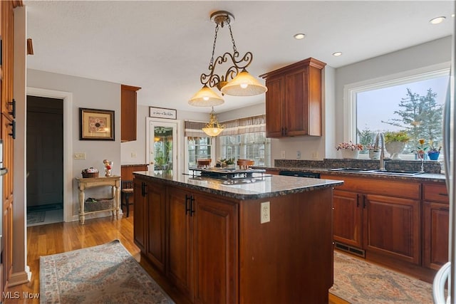 kitchen with hanging light fixtures, sink, light hardwood / wood-style floors, a kitchen island, and stainless steel gas cooktop