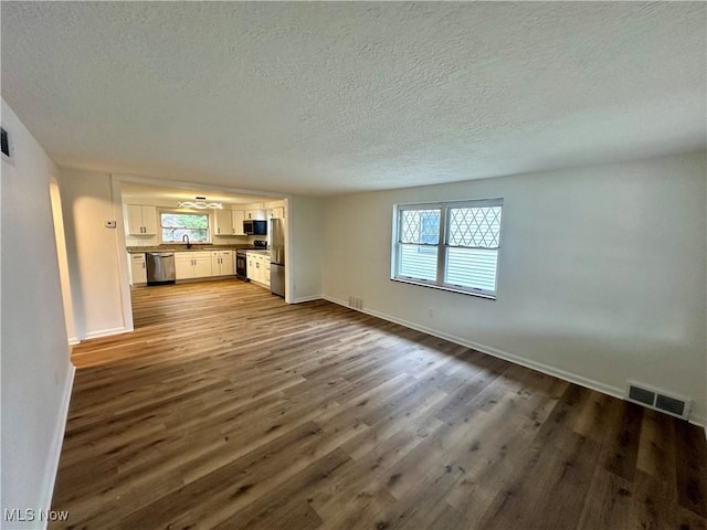 unfurnished living room featuring a textured ceiling, dark hardwood / wood-style flooring, plenty of natural light, and sink