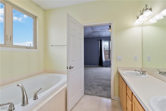 bathroom featuring vanity, a wealth of natural light, ceiling fan, and a relaxing tiled tub