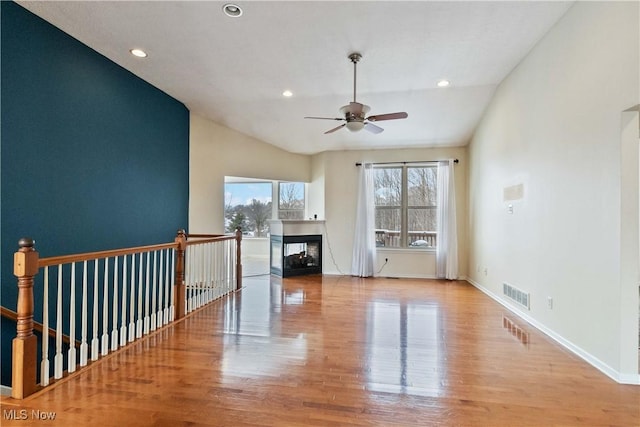 unfurnished living room featuring a multi sided fireplace, ceiling fan, vaulted ceiling, and light wood-type flooring