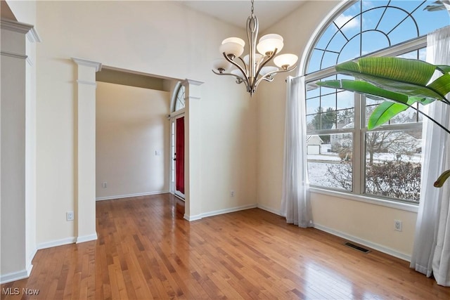 unfurnished dining area featuring ornate columns, a notable chandelier, vaulted ceiling, and hardwood / wood-style flooring