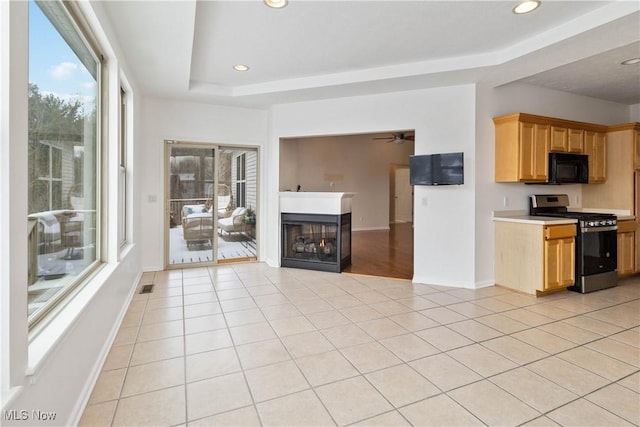 kitchen featuring a tray ceiling, stainless steel range with gas cooktop, light tile patterned floors, and a multi sided fireplace