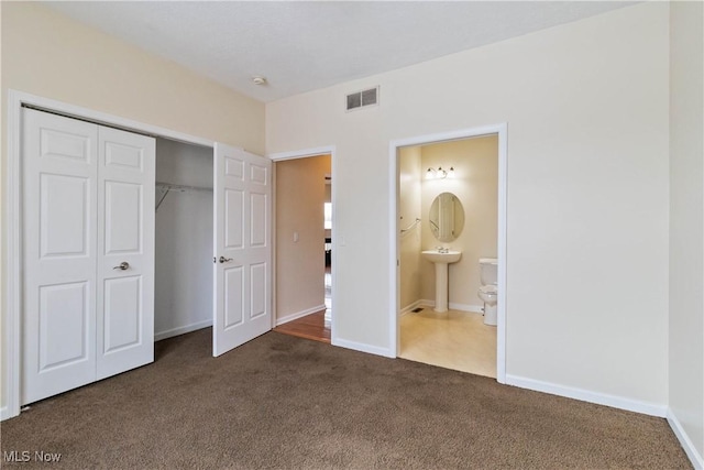 unfurnished bedroom featuring ensuite bathroom, a closet, sink, and dark colored carpet