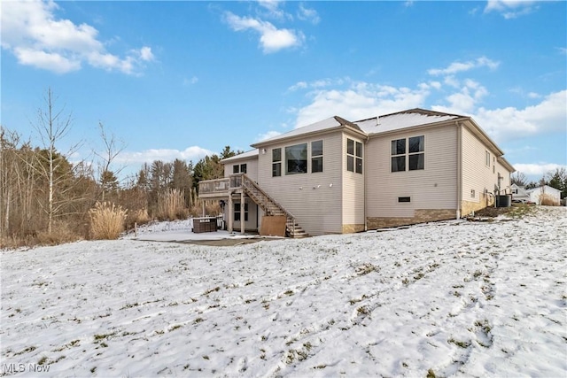 snow covered back of property with central air condition unit and a deck