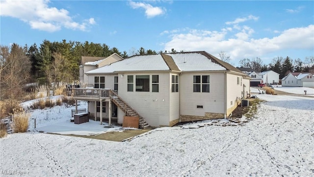 snow covered back of property with a hot tub and a deck