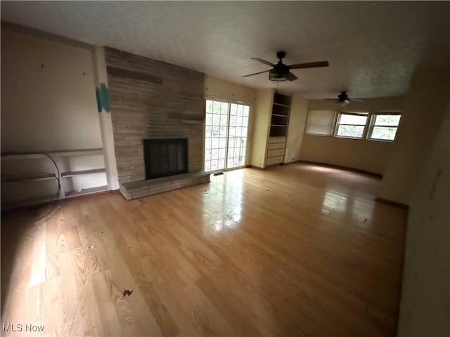 unfurnished living room with a large fireplace, ceiling fan, and light hardwood / wood-style flooring