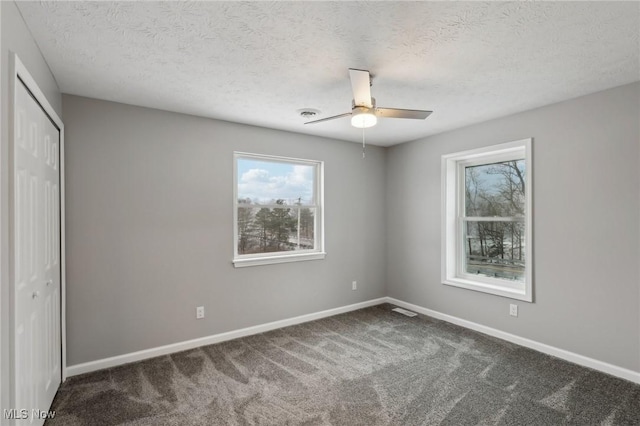 unfurnished bedroom featuring dark colored carpet, a textured ceiling, a closet, and ceiling fan