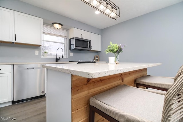 kitchen with stainless steel appliances, a kitchen island, a kitchen breakfast bar, light hardwood / wood-style flooring, and white cabinets