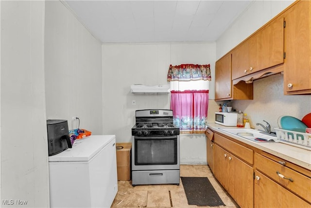 kitchen featuring light tile patterned flooring, washer / dryer, stainless steel gas range oven, and sink