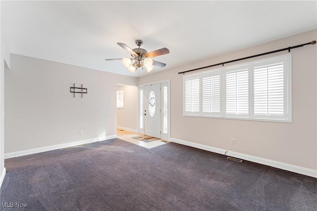 unfurnished room with dark colored carpet, a wealth of natural light, and ceiling fan