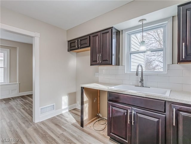 kitchen with sink, light hardwood / wood-style floors, decorative light fixtures, decorative backsplash, and dark brown cabinets