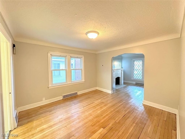 spare room featuring a fireplace, a textured ceiling, light hardwood / wood-style floors, and crown molding