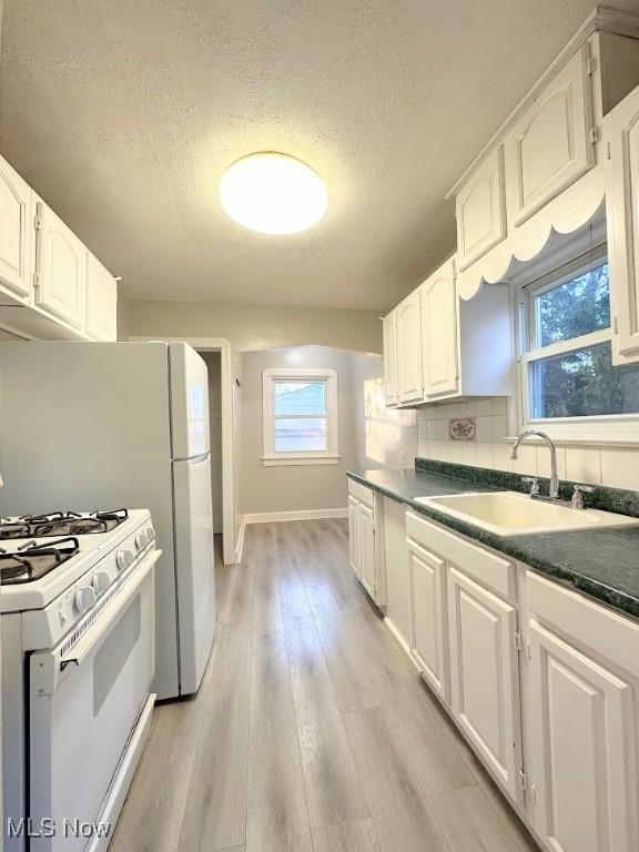 kitchen with white appliances, white cabinetry, sink, and light hardwood / wood-style flooring