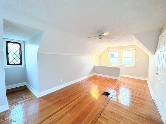 additional living space with a textured ceiling, ceiling fan, light hardwood / wood-style floors, and vaulted ceiling