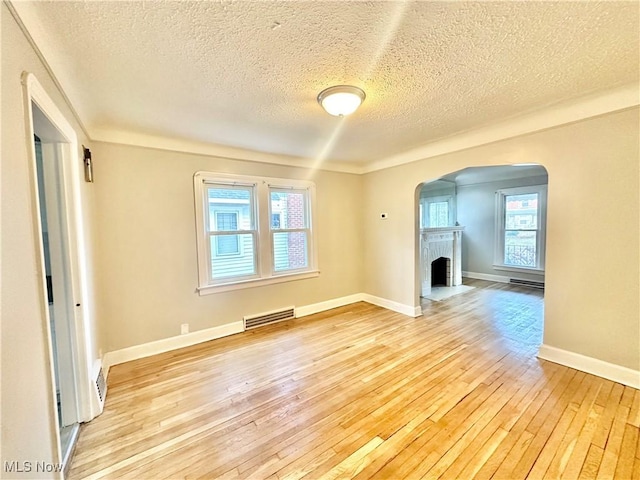 unfurnished living room featuring light wood-type flooring, a textured ceiling, and a brick fireplace