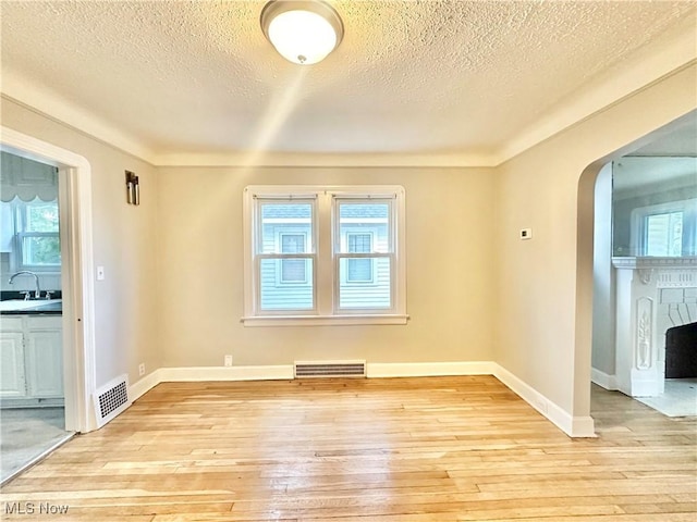 unfurnished room featuring a textured ceiling, light wood-type flooring, sink, and a brick fireplace