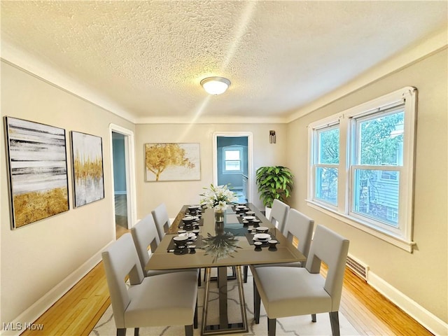 dining area with crown molding, a textured ceiling, and light hardwood / wood-style flooring