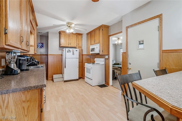 kitchen with white appliances, sink, wooden walls, ceiling fan, and light hardwood / wood-style floors