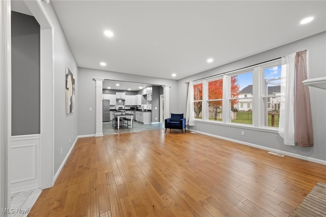 unfurnished living room featuring decorative columns, plenty of natural light, and light wood-type flooring