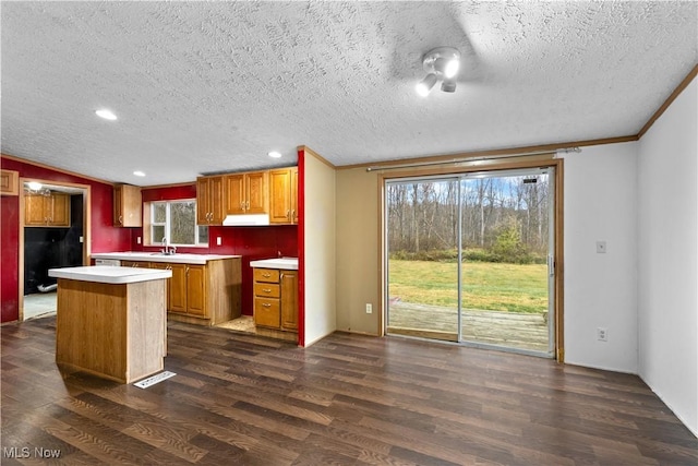 kitchen featuring crown molding, a kitchen island, dark wood-type flooring, and a textured ceiling