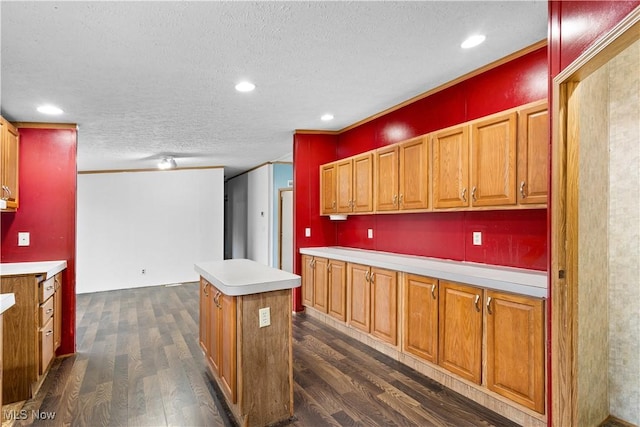 kitchen with a textured ceiling, dark hardwood / wood-style floors, a kitchen island, and ornamental molding