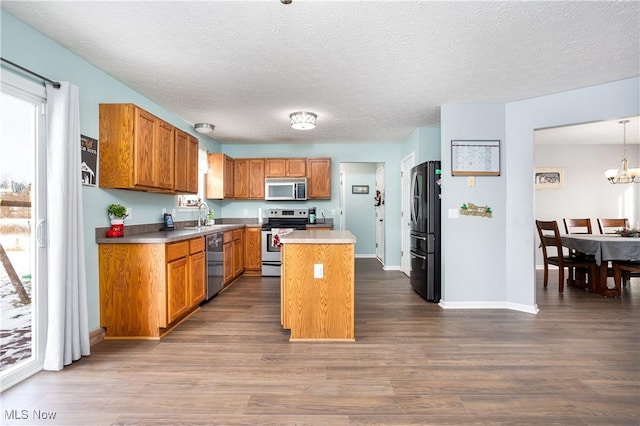 kitchen featuring stainless steel appliances, dark wood-type flooring, sink, a kitchen island, and hanging light fixtures