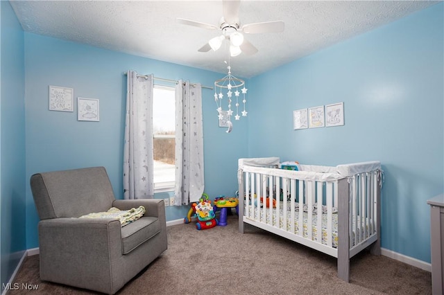 carpeted bedroom featuring ceiling fan, a textured ceiling, and a nursery area