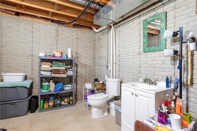 bathroom with vanity, toilet, and brick wall