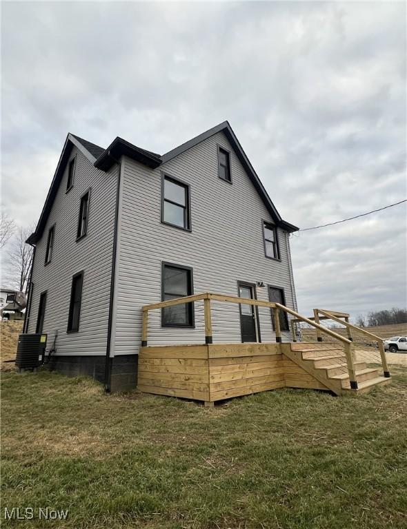 back of property with a yard, a deck, and central AC unit