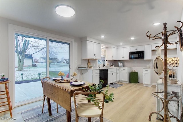 kitchen featuring sink, backsplash, light hardwood / wood-style floors, white cabinets, and black appliances