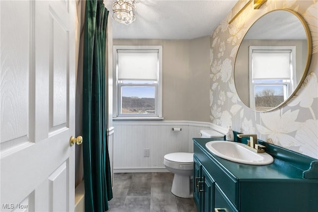 bathroom with wallpapered walls, wainscoting, toilet, a textured ceiling, and vanity