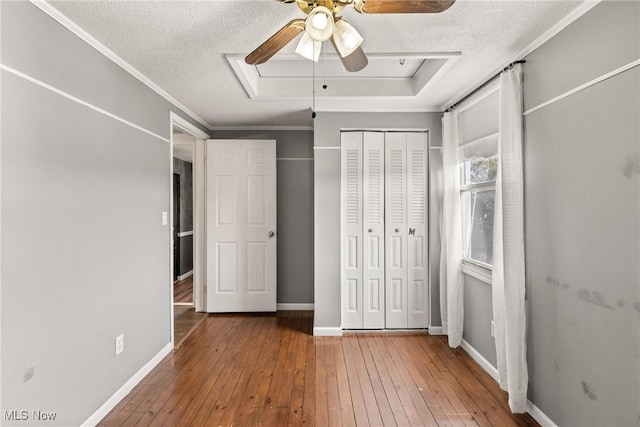 unfurnished bedroom featuring a textured ceiling, a tray ceiling, wood finished floors, and baseboards