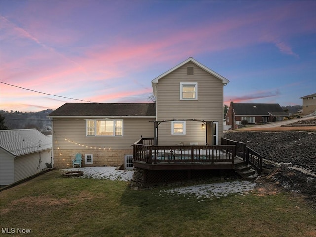 back of house at dusk featuring a deck and a lawn