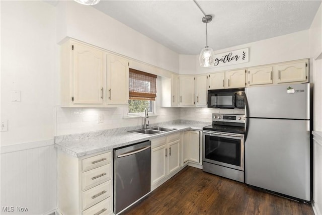 kitchen featuring stainless steel appliances, a sink, hanging light fixtures, light countertops, and wainscoting