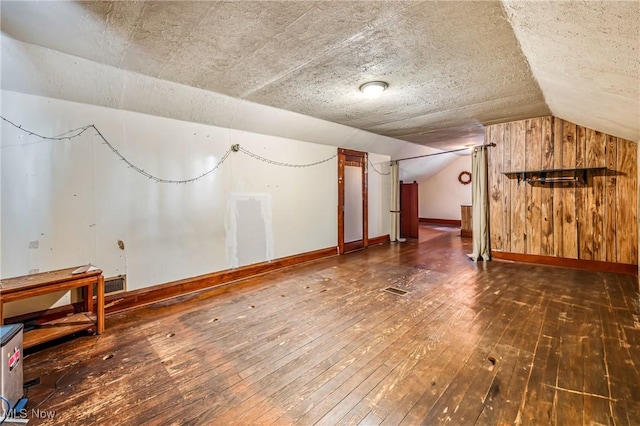 additional living space featuring a textured ceiling, lofted ceiling, dark wood-type flooring, and wooden walls